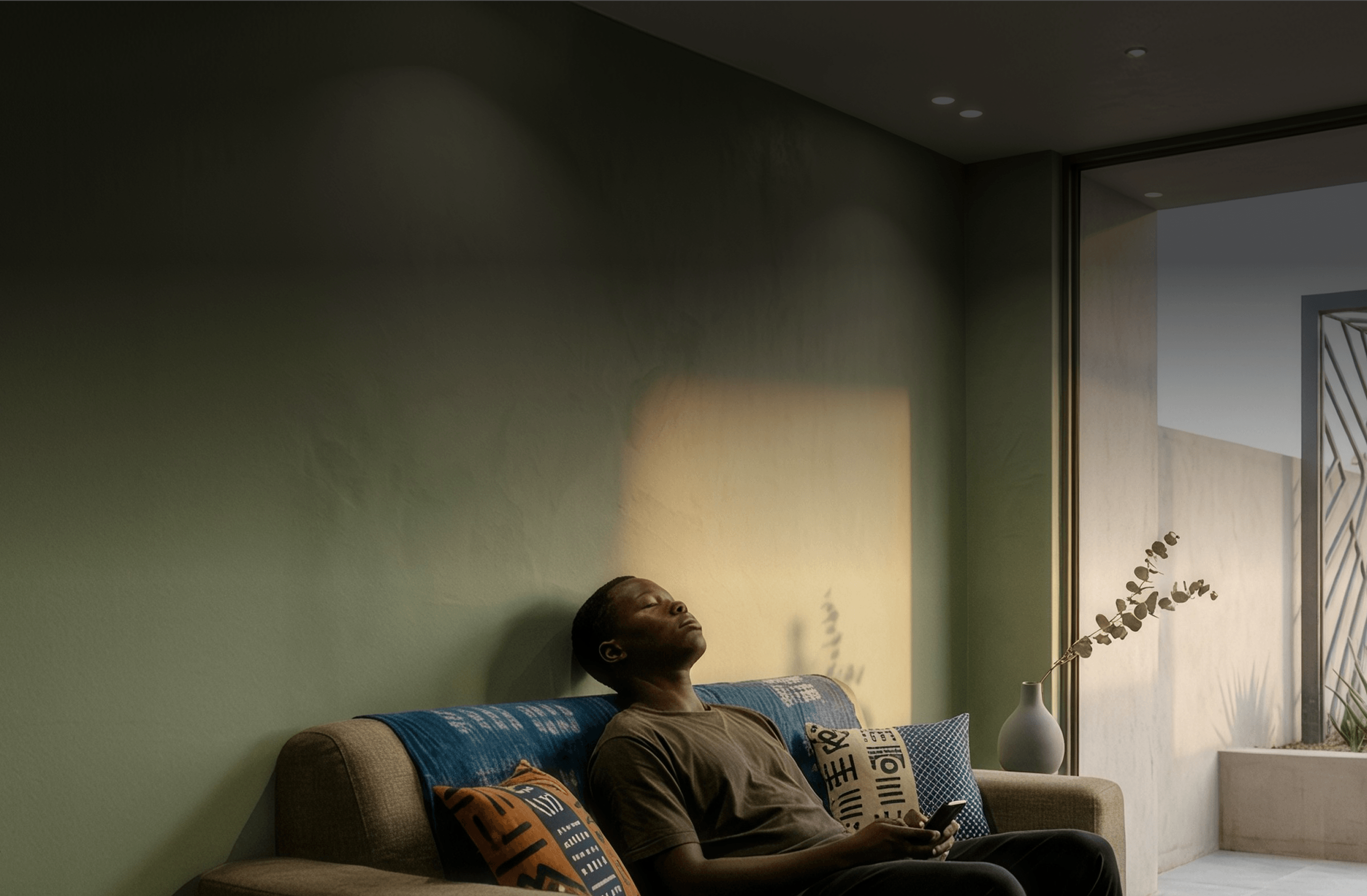 A man resting on a sofa with his eyes closed in a softly lit room